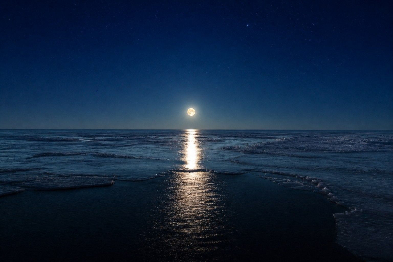 A full moon low over a frozen Arctic sea, laying a narrow silver path across thin new ice with a strip of open black water in the foreground under a deep indigo sky.